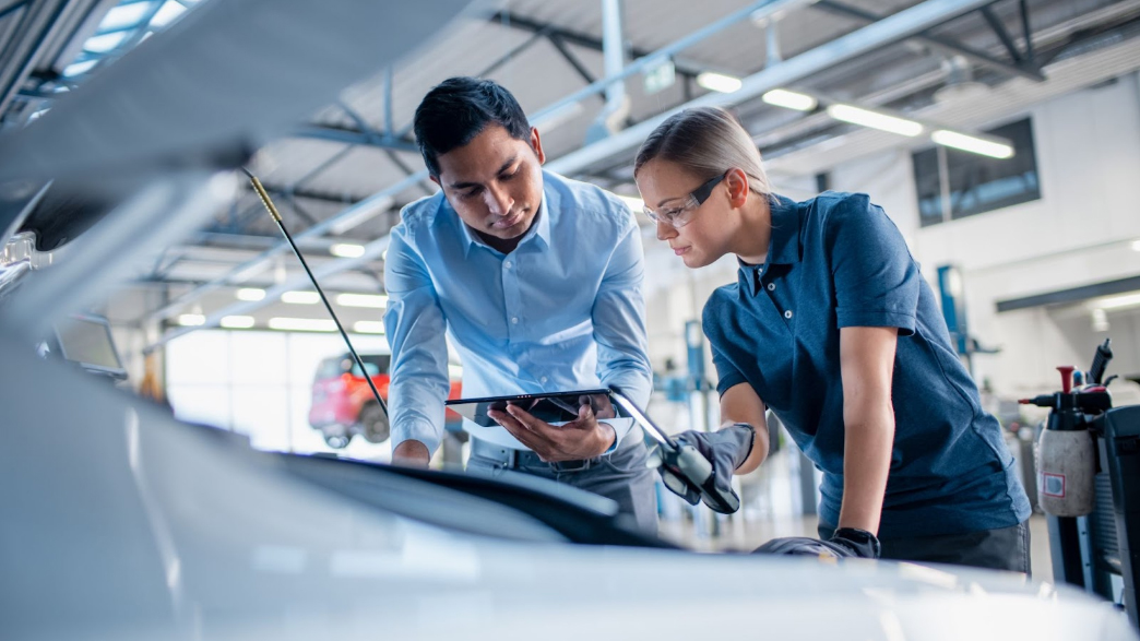 In a repair shop, two mechanics inspect engine data on a tablet, potentially diagnosing a 2022 Suburban metal in oil issue.
