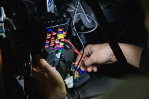 Hands working on a vehicle fuse box and wiring under the dashboard, illustrating common 2025 Ford Expedition problems. 